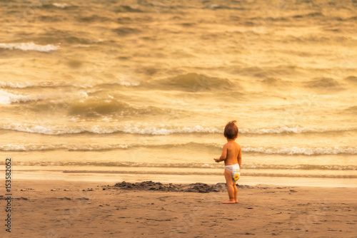 Baby in diapers are looking at the sea skeptically on the beach in the evening, the concept of learning.