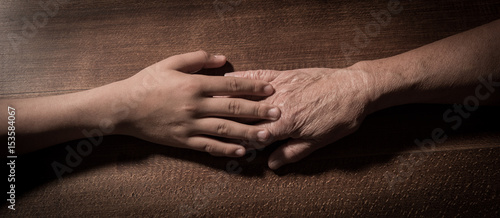 Child hands holding senior woman's hands on brown background