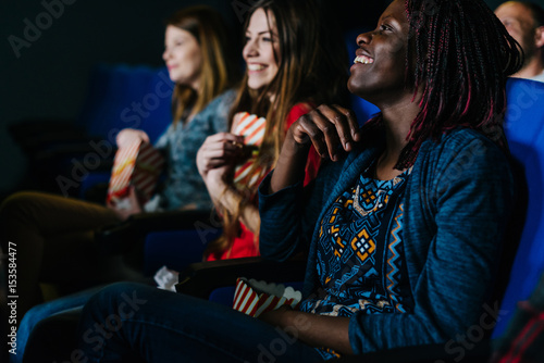 Smiling black woman watching a movie in good company at the cinema