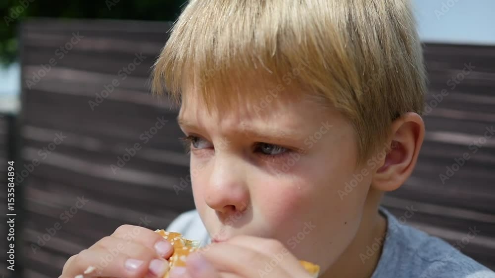 A child eats a bun with a cutlet and cheese in a fast food restaurant A child eats a bun with a cutlet and cheese in a fast food restaurant