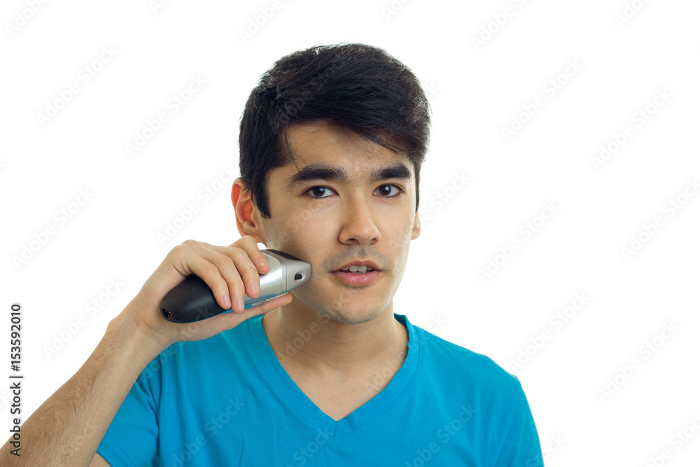 Chic young guy looks straight and shaves a beard trimmer close-up Chic young guy looks straight and shaves a beard trimmer close-up