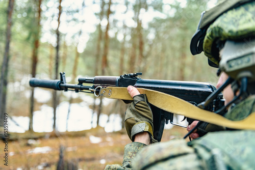 Automatic weapons in the hands of a soldier of the Russian army during a combat operation, against a background of coniferous forest and field