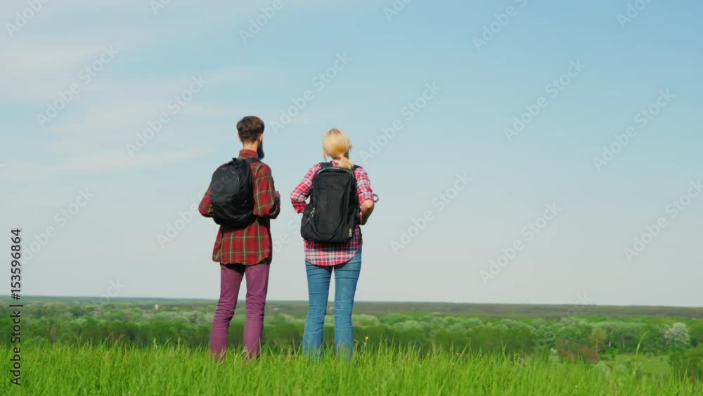 A man and a woman with backpacks standing at the edge of a large green hill or mountain. Looking forward to the horizon. Steadicam fly around video A man and a woman with backpacks standing at the edge of a large green hill or mountain. Looking forward to the horizon. Steadicam fly around video