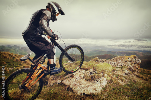 Tablou pe pânză Ryder in full protective equipment on the mtb bike climbs on a rock against the