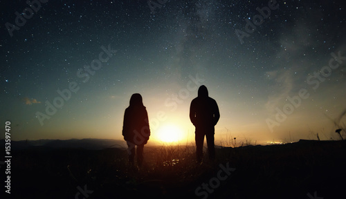 A couple of people man and woman stand at the sunset of the moon under the starry sky with bright stars and a milky way. Silhouetted photo against the starry night sky