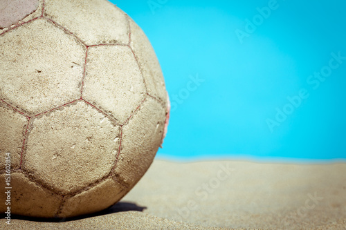un vieux ballon sur du sable avec un fond bleu