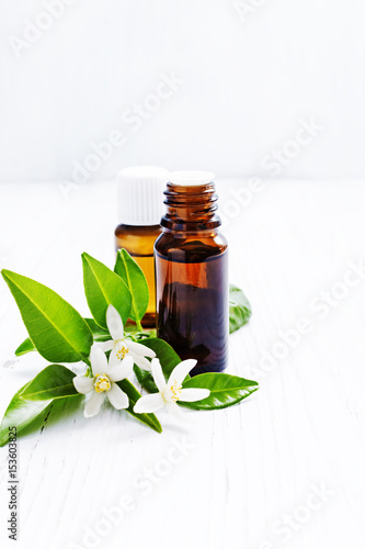 Neroli (Citrus aurantium) essential oil in a brown glass bottle with fresh white  flowers on ligth background. Selective focus.