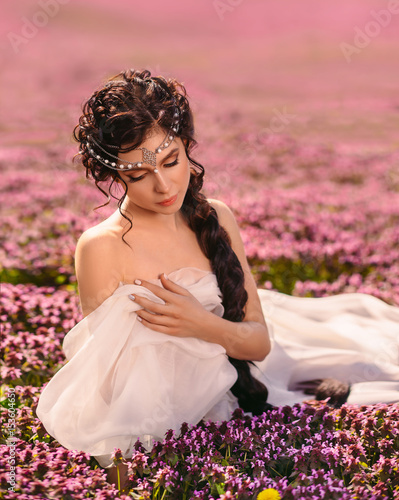 A beautiful girl in a white dress. Long hair is tightly braided. The Greek goddess is resting in a field of flowers.