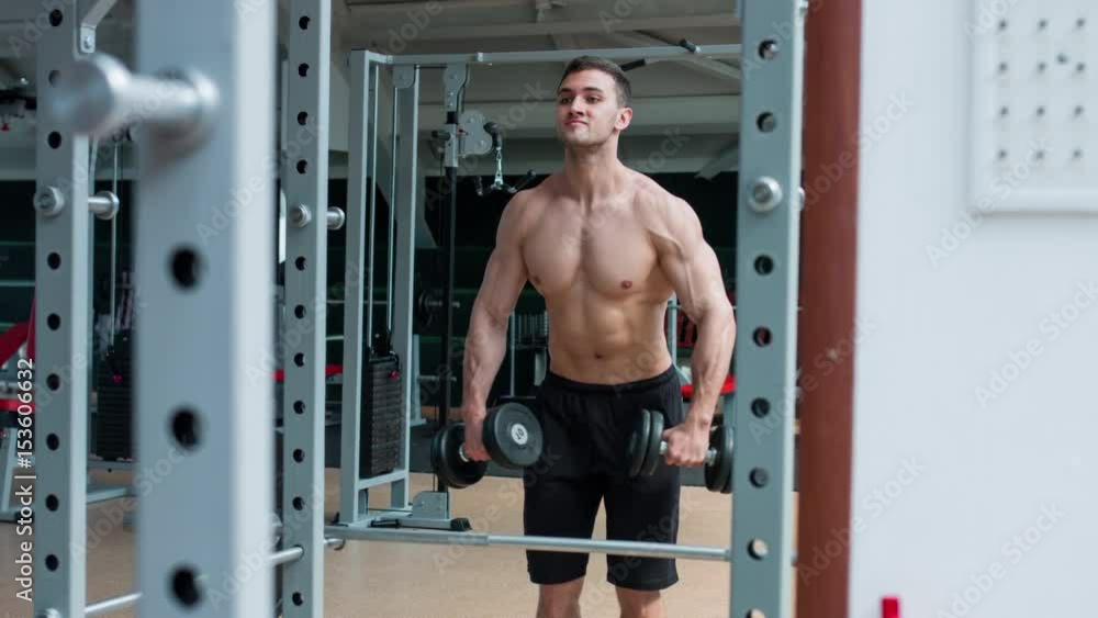 Man working his arms at the gym. He lifting the dumbbells and working his biceps. Naked torso. Man working his arms at the gym. He lifting the dumbbells and working his biceps. Naked torso.