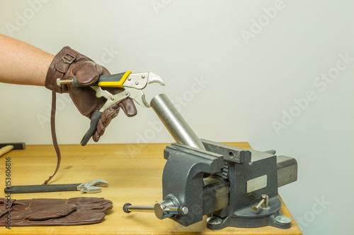 Caucasian hands in brown leather gloves fixing a pipe with a circular flat cutting pliers wrench hold by a vise on a working bench