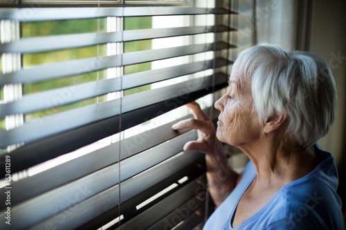 Fotografie Senior woman looking out from window blind