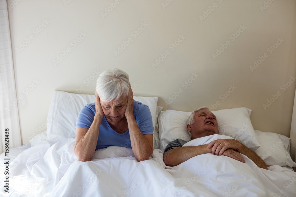 Senior woman getting disturbed with man snoring on bed Senior woman getting disturbed with man snoring on bed