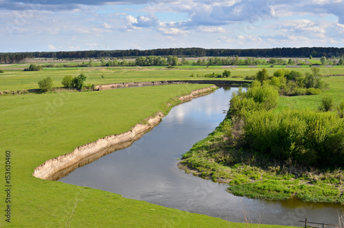 Spring landscape with river bending between vibrant green meadows. Top view. Beautiful nature scenery.