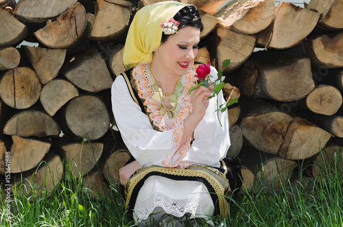 beautiful young smiling woman crouching next to the wood in the countryside and smell a rose photo