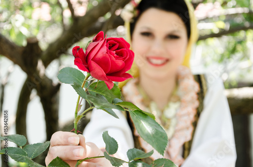 beautiful young smiling woman or girl gives rose to the camera outdoors