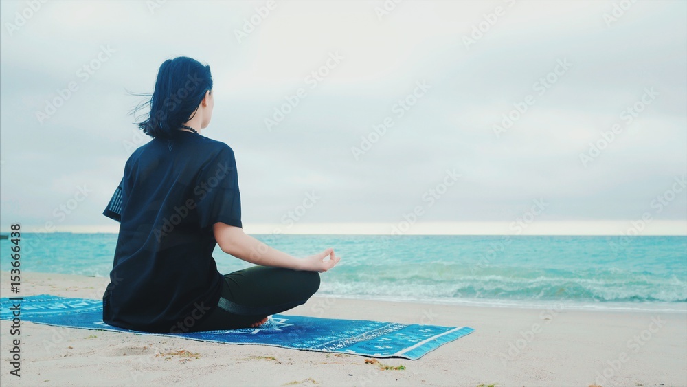 Fitness woman in sports clothing practicing yoga on the sea ocean beach close up to water. Dolly shot. Calm young woman sitting in lotus pose.