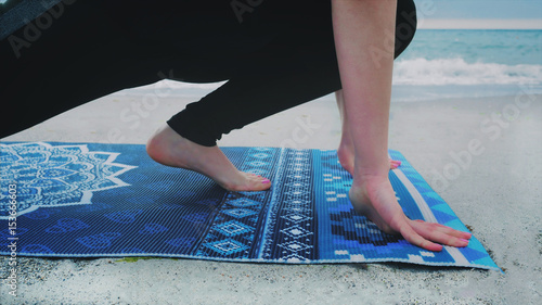CLose up down view of female legs doing yoga and stretching on a blue mat with mandala on the sea or ocean beach.