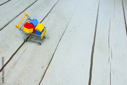 House and building toys inside shopping cart over wooden background