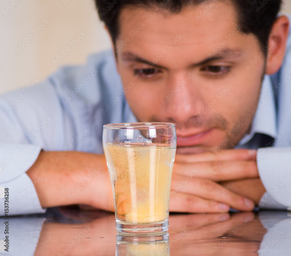 Handsome man watching an effervescent tablet in glass of water dissolving Handsome man watching an effervescent tablet in glass of water dissolving