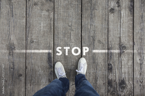 Man standing on the wooden boards with stop message on the floor, point of view perspective used.