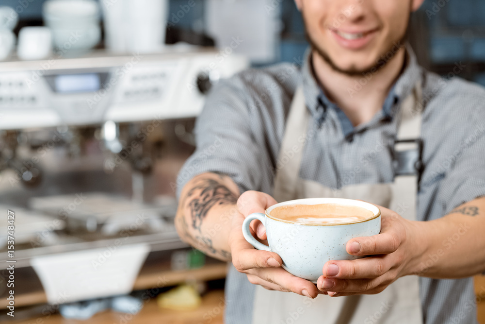 Just for you. Cropped closeup of a smiling male barista giving a cup of coffee to the viewer Just for you. Cropped closeup of a smiling male barista giving a cup of coffee to the viewer