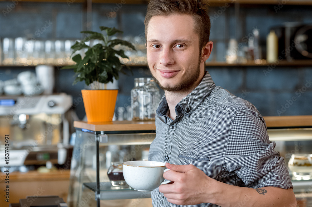 Quality checked personally. Shot of a young hipster man smiling to the camera holding a cup of coffee at the local coffee shop Quality checked personally. Shot of a young hipster man smiling to the camera holding a cup of coffee at the local coffee shop