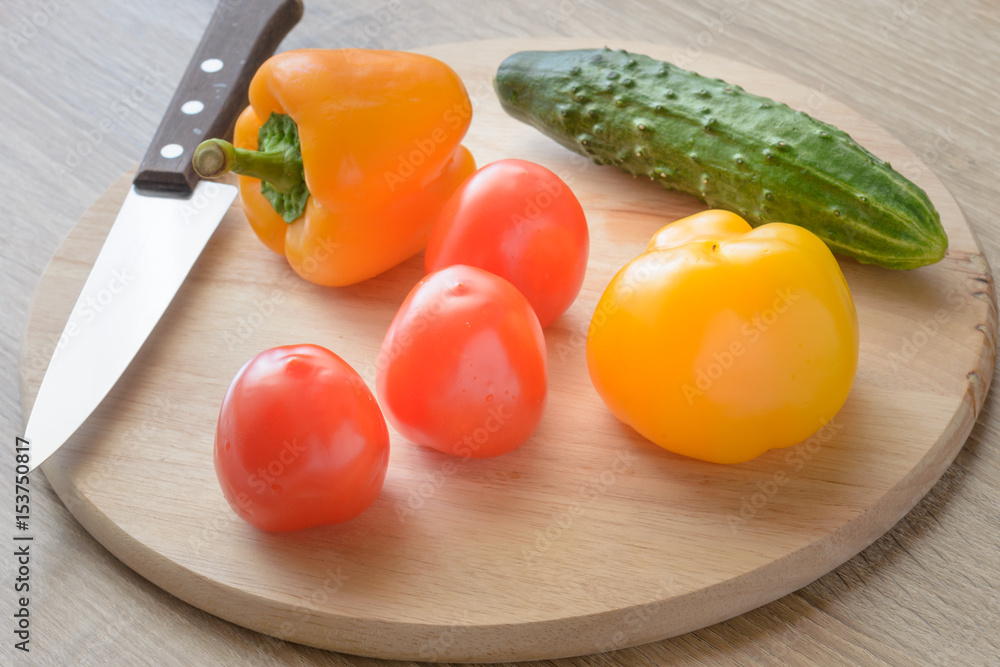 Tomatoes and cucumbers and peppers on a cutting board.