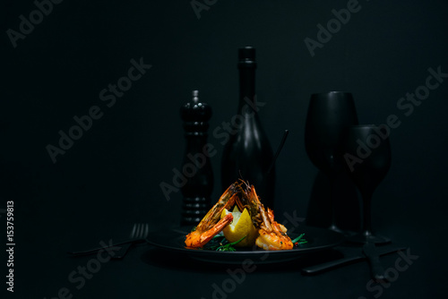 fried shrimps with lemon on black background with wine glass and wine bottle