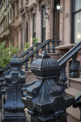 Close up of a decorative railing on a stoop in front of a row of traditional brownstones on a historic block in Brooklyn, New York City