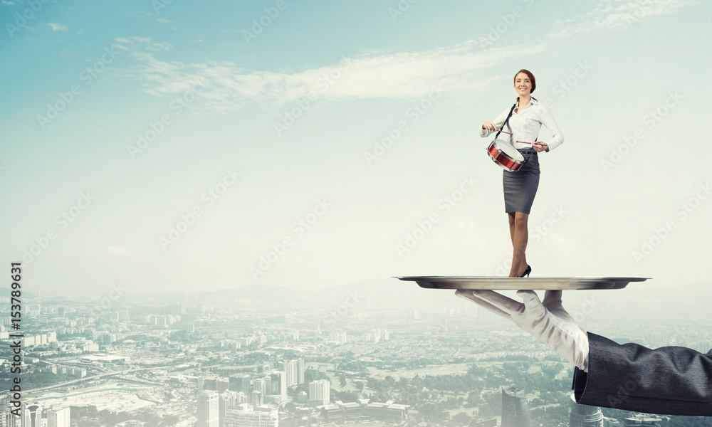 Attractive businesswoman on metal tray playing drums against cityscape background Attractive businesswoman on metal tray playing drums against cityscape background