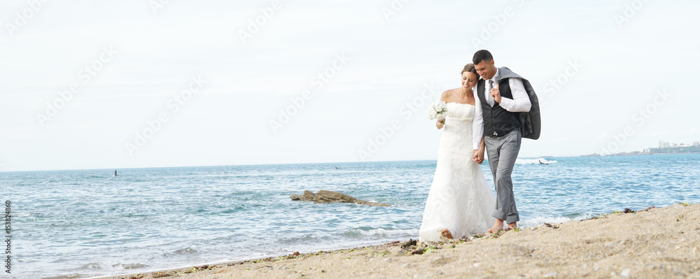Happy bride and groom walking on beach at sunset Happy bride and groom walking on beach at sunset