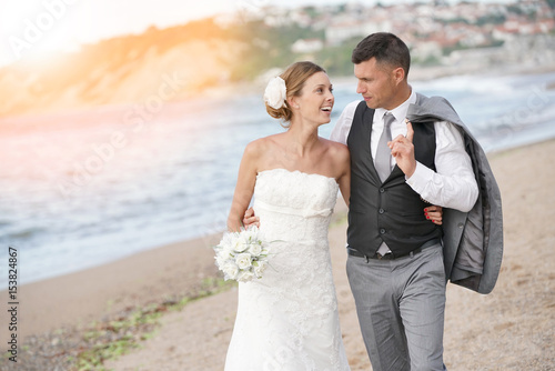 Happy bride and groom walking on beach at sunset © goodluz