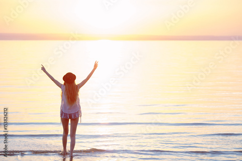 Silhouette of woman wearing hat with open arms under the sunrise near the sea