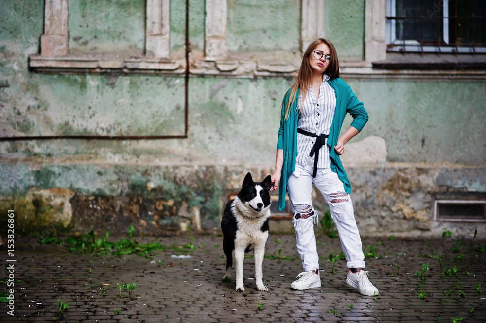 Trendy girl at glasses and ripped jeans with russo-european laika (husky) dog on a leash, against street of city. Friend human with animal theme. Trendy girl at glasses and ripped jeans with russo-european laika (husky) dog on a leash, against street of city. Friend human with animal theme.