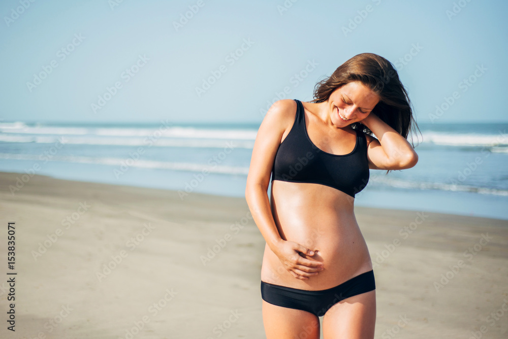 Portrait of beautiful happy dark-hear pregnant woman in black bikini on the beach Portrait of beautiful happy dark-hear pregnant woman in black bikini on the beach