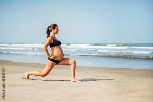 Pregnant woman on the beach doing yoga. Pregnant woman doing workout near the the sea.