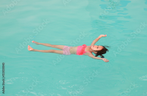 Little girl floating on the water surface of the swimming pool.