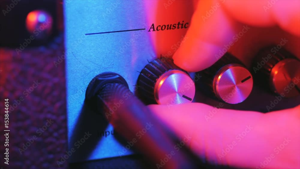 Men's hands twist tumblers on control panel of guitar amplifier. A mode switch being switches on amp. Man's hand inserts cable jack in guitar amp. Neon light, Concert.