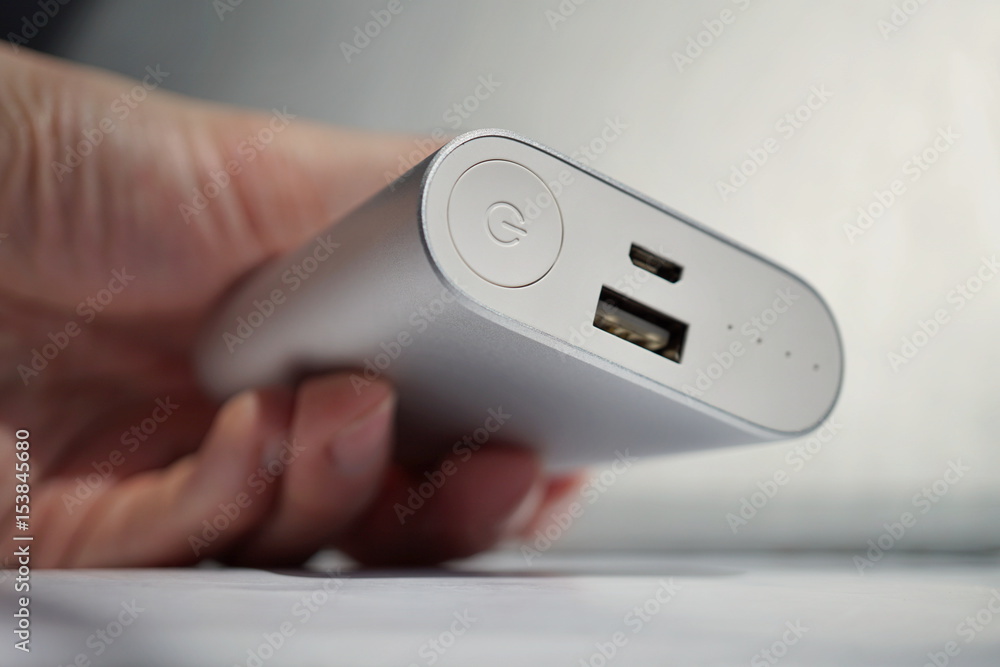 Male hand holding a silver aluminum power bank in modern slick design used as an external source of energy Male hand holding a silver aluminum power bank in modern slick design used as an external source of energy