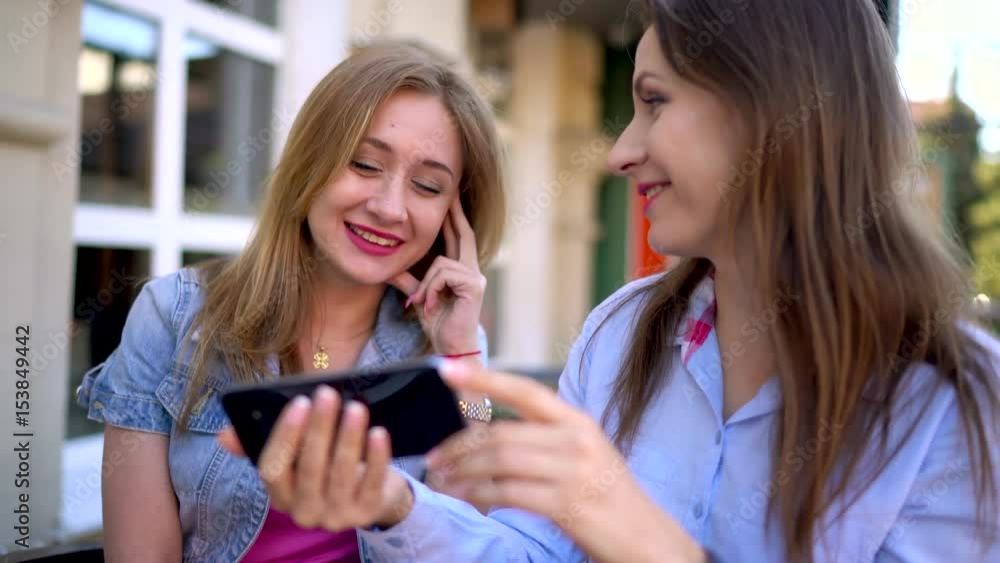 Two cheerful women talk and use a smartphone in a cafe Two cheerful women talk and use a smartphone in a cafe