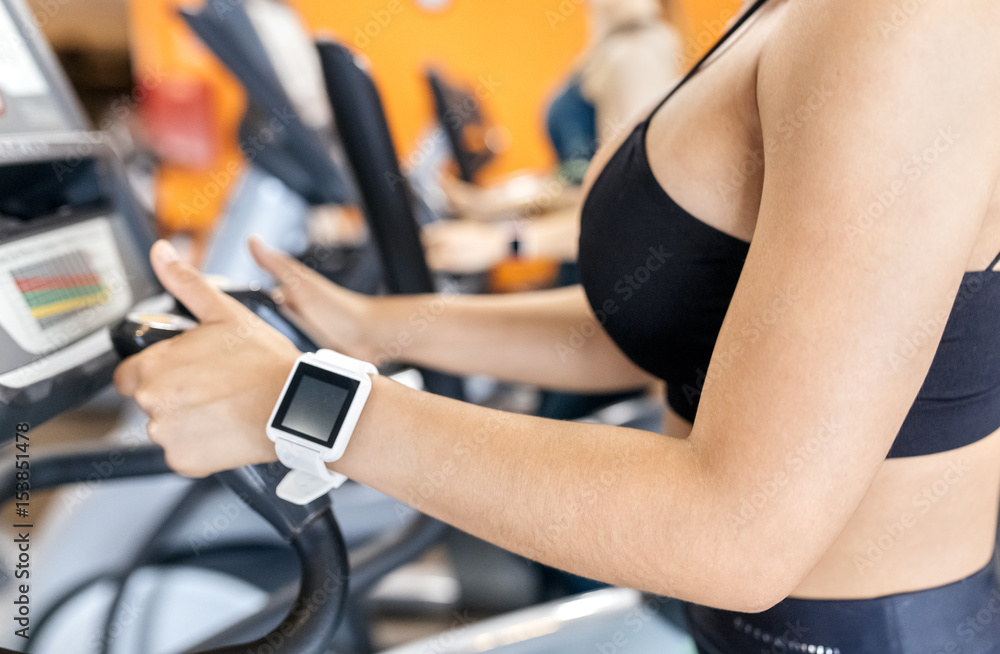 Woman in gym with smartwatch using an elliptical trainer Woman in gym with smartwatch using an elliptical trainer