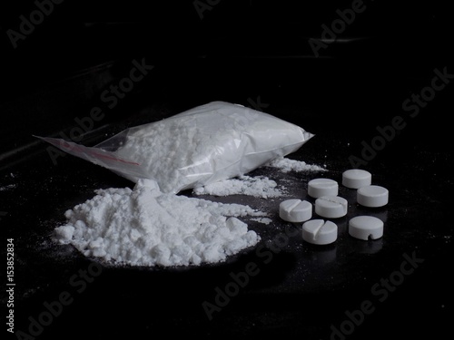 Cocaine drug powder bag and pile and pills on black background