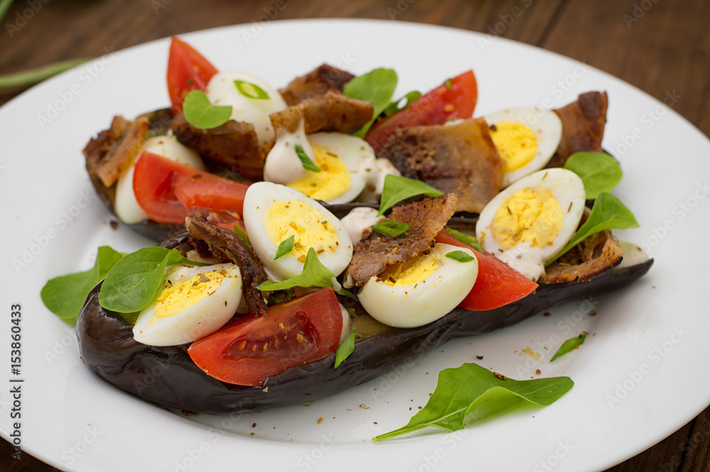 Baked eggplant with bacon, garlic and quail eggs. Wooden background. Top view. Close-up Baked eggplant with bacon, garlic and quail eggs. Wooden background. Top view. Close-up