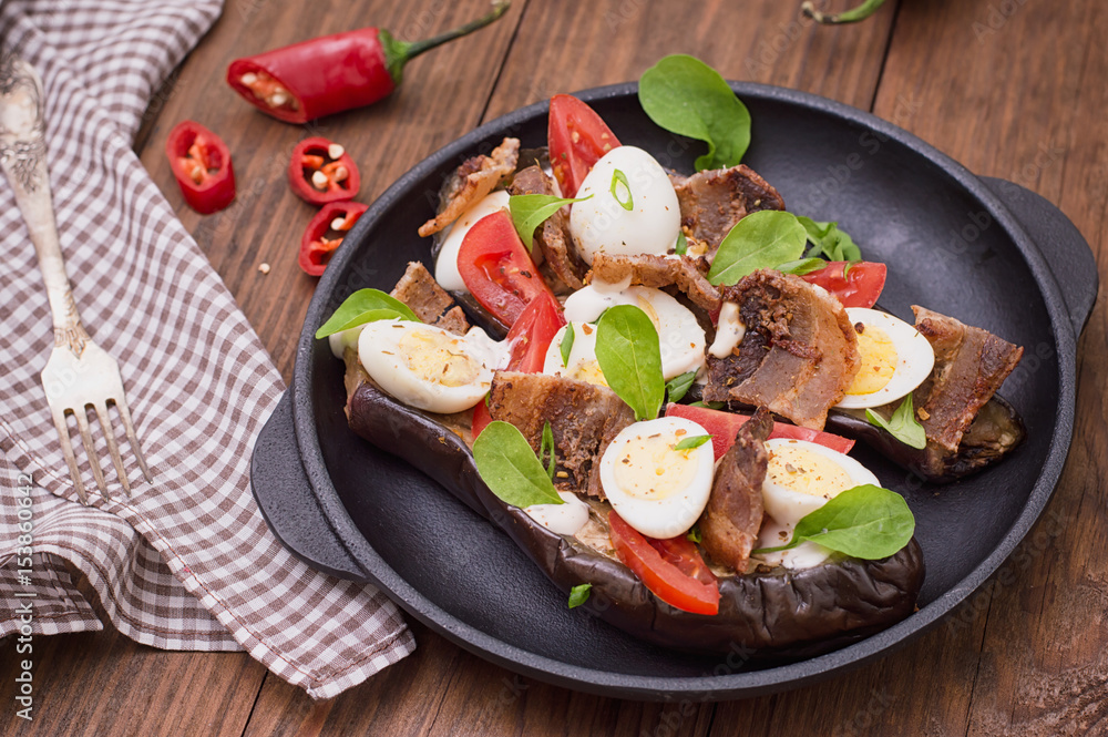 Baked eggplant with bacon, garlic and quail eggs on pan. Wooden background. Top view. Close-up
