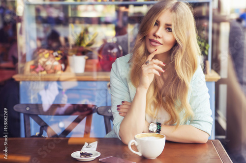 Beautiful rich casual blonde stylish fashion business woman with a phone  working in blue jacket and colorful skirt at the cafe table drinking coffee. European cafe on a background