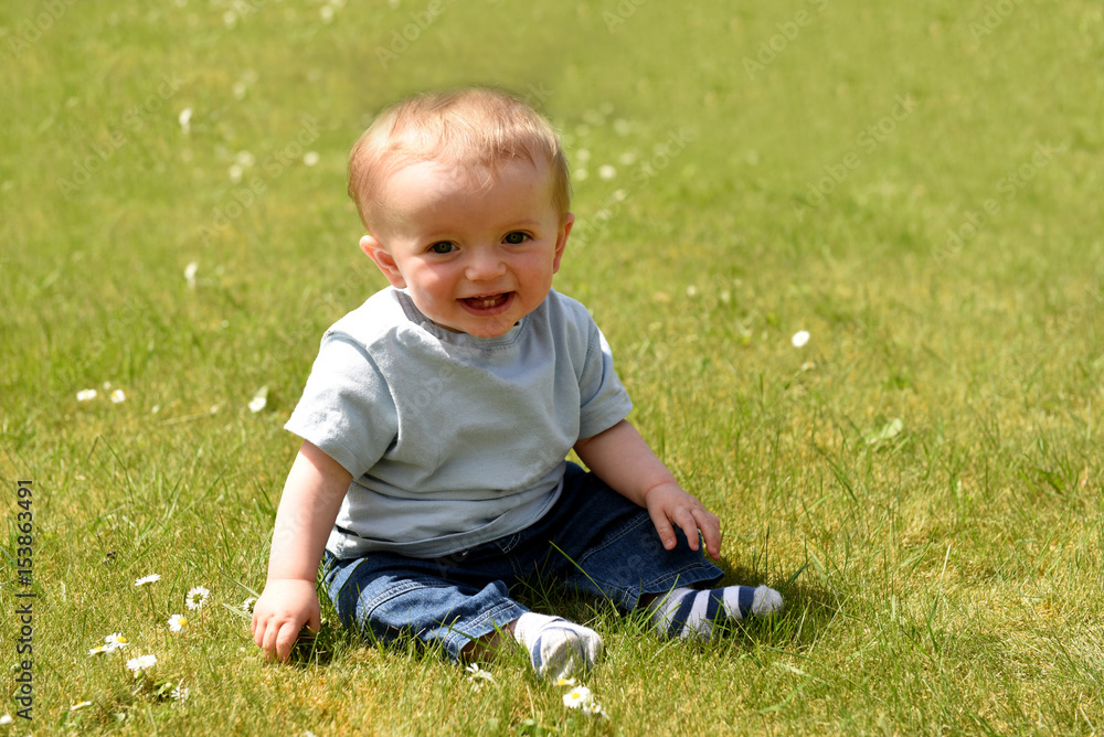 Happy ten month old baby boy sitting down outdoors on a sunny day Happy ten month old baby boy sitting down outdoors on a sunny day