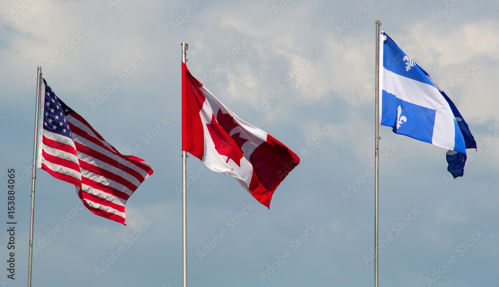 Fototapeta premium Canada, USA, and Quebec flags waving in the wind cloudy day