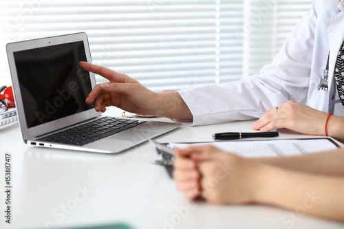 Close-up of a doctor and patient sitting at the desk while physician pointing into laptop computer. Medicine and health care concept