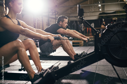 Sportsmen doing exercises with?rowing machine together