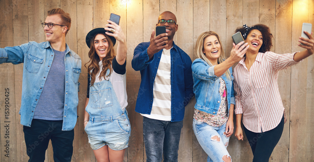 Fototapeta premium Happy multiethnic friends taking selfie at wooden wall